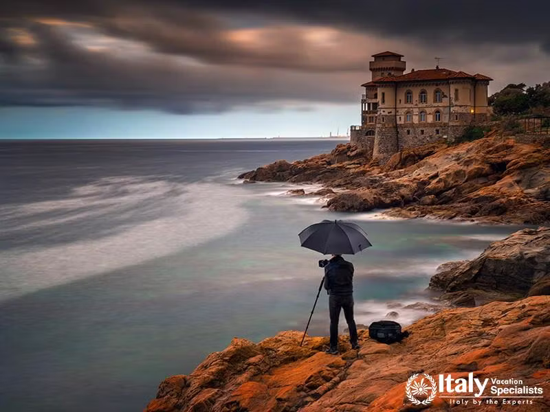 Photographer with umbrella at Boccale Castle on rocky coastline near Livorno, Italy