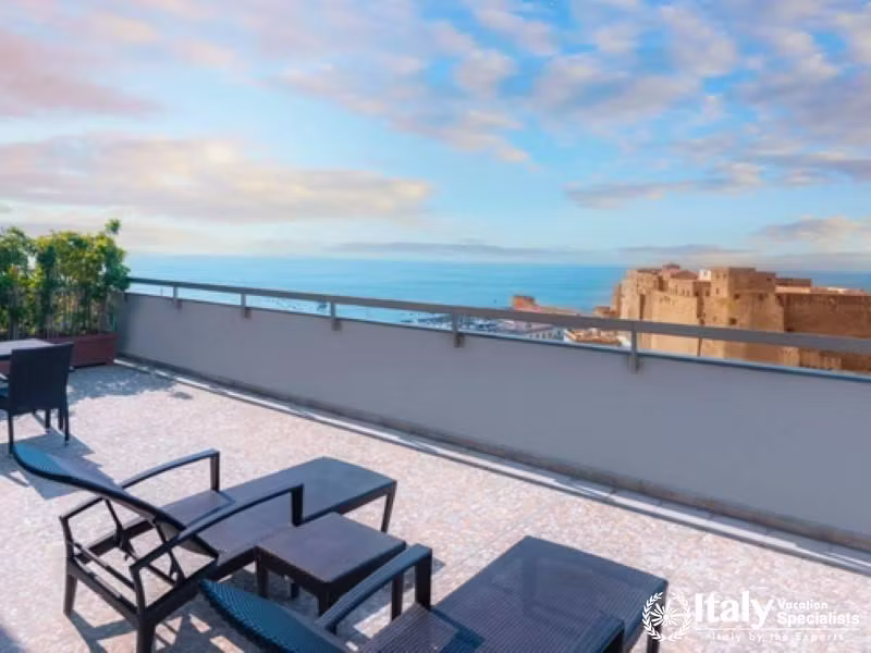 A balcony with comfortable seating and breathtaking views of the sea and castle.