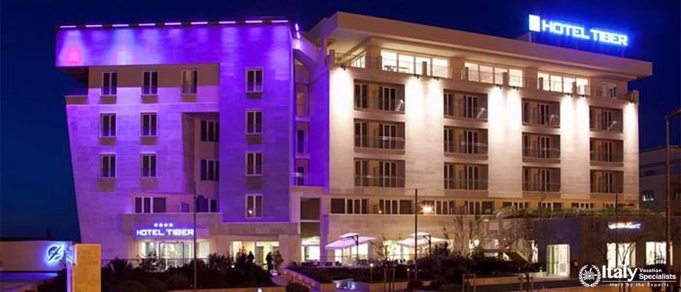The exterior of Hotel Tiber illuminated at night, showcasing its modern architecture.