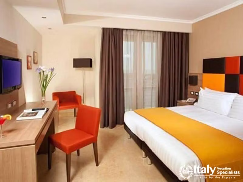 A modern hotel room with a bright yellow bedspread, red chairs, and a balcony.