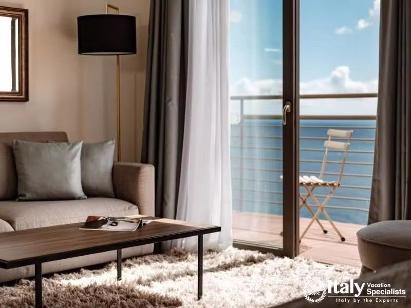 A cozy sitting area with a sofa, coffee table, and a balcony offering a view of the sea.