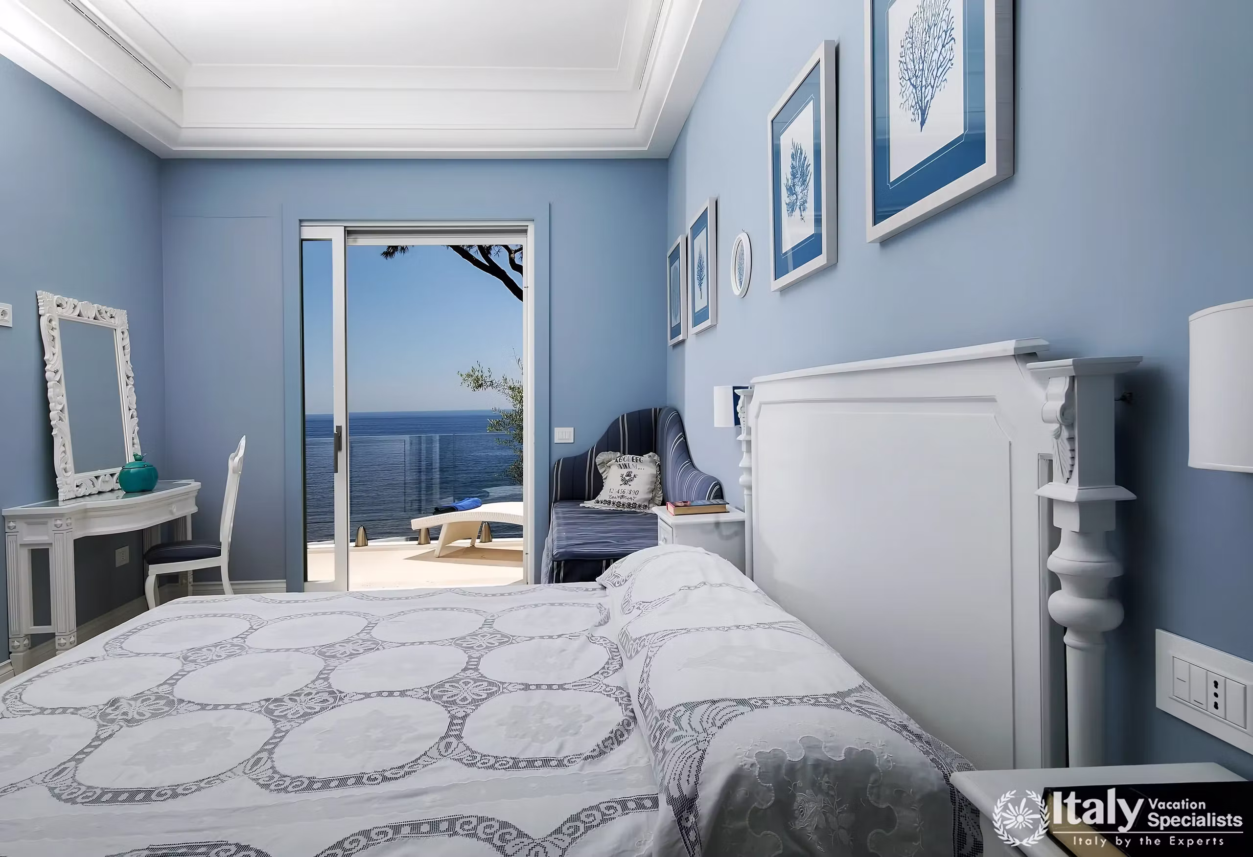 Blue double bedroom at Villa Mare Meraviglioso with a white lace bedspread and a glass door opening to a sea view terrace