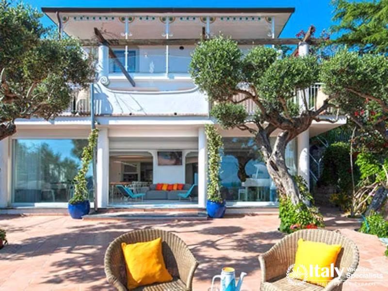 The beautiful front facade of the villa with a spacious patio and outdoor seating.