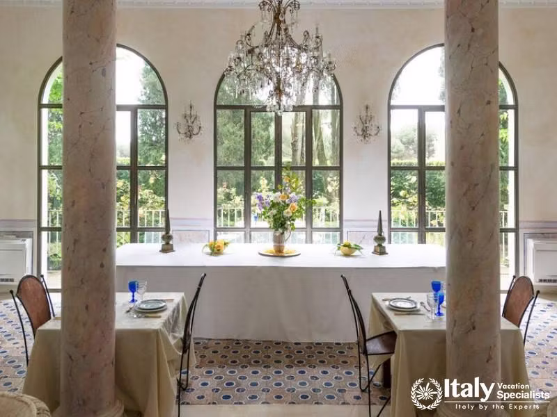 Elegant dining room with chandeliers and large windows overlooking greenery.