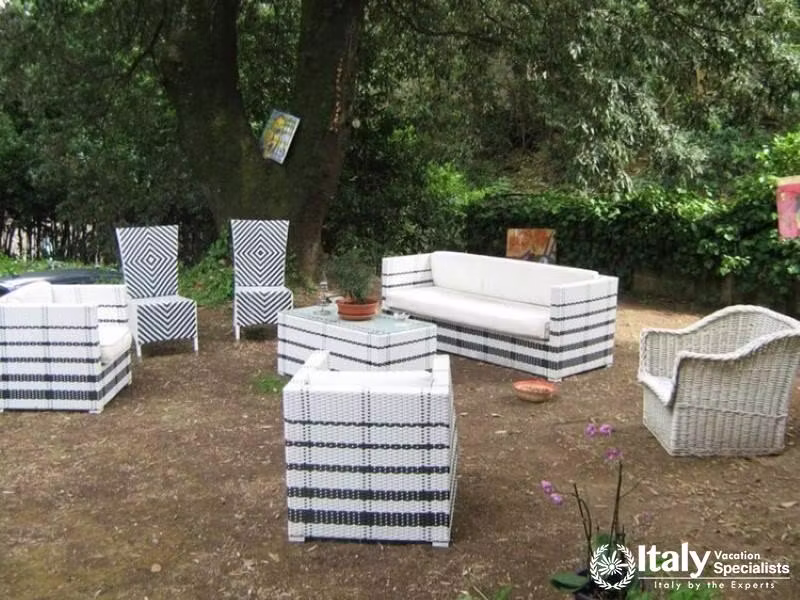 An outdoor seating area with modern white and black wicker furniture set under a large tree.