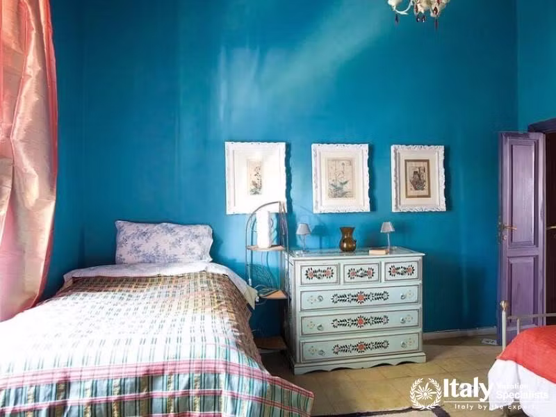 A cozy bedroom painted in a vibrant blue with a single bed and a decorative dresser.