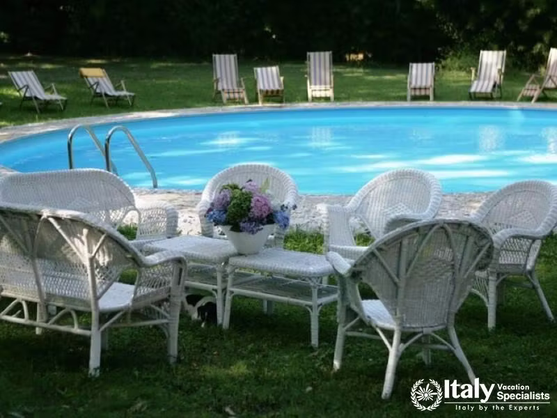 A serene pool area with white wicker furniture arranged for relaxation.