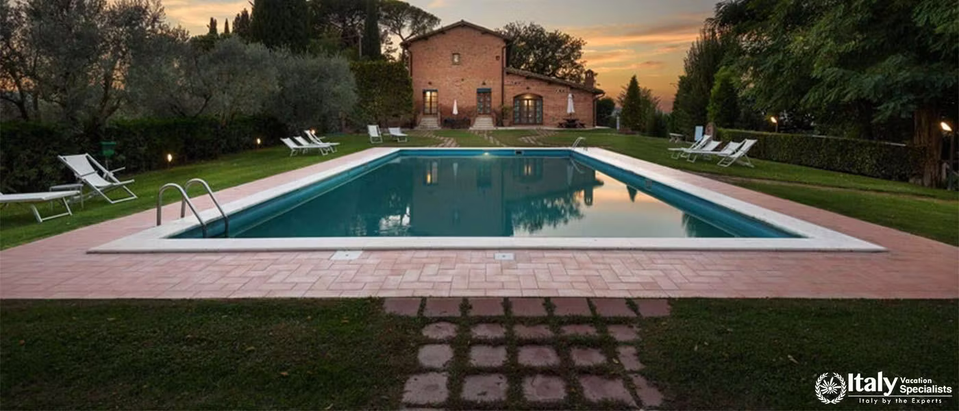 A Tuscan villa and pool illuminated by evening light.