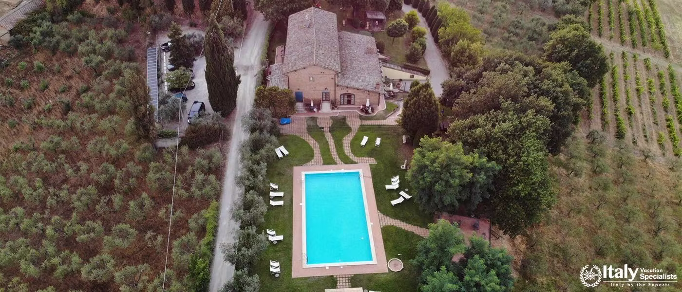 An overhead view of a charming villa with a swimming pool surrounded by gardens and orchards.