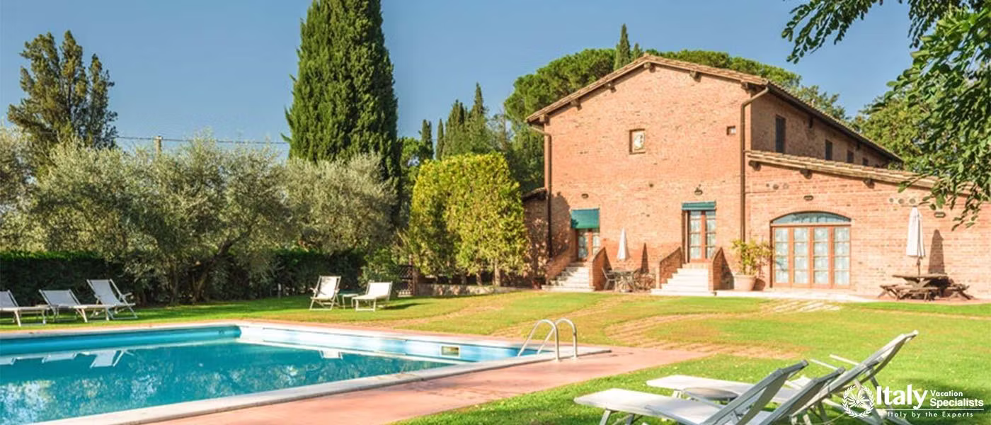 A classic Tuscan villa with a long swimming pool flanked by olive trees and sun loungers.
