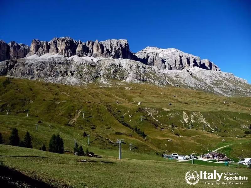 A sweeping view of Passo Pordoi, surrounded by rolling green hills and dramatic mountain peaks.