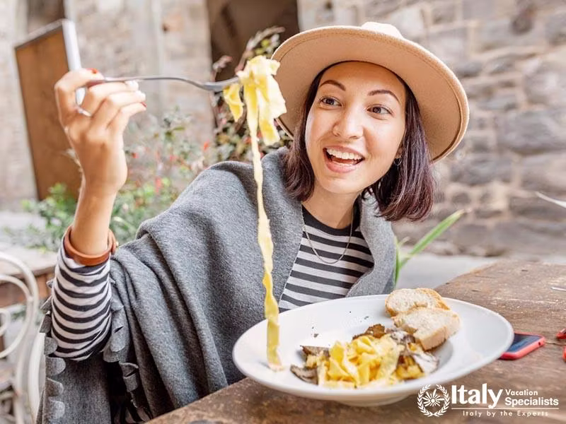 Happy asian woman eating pasta with truffle in outdoor italian restaurant