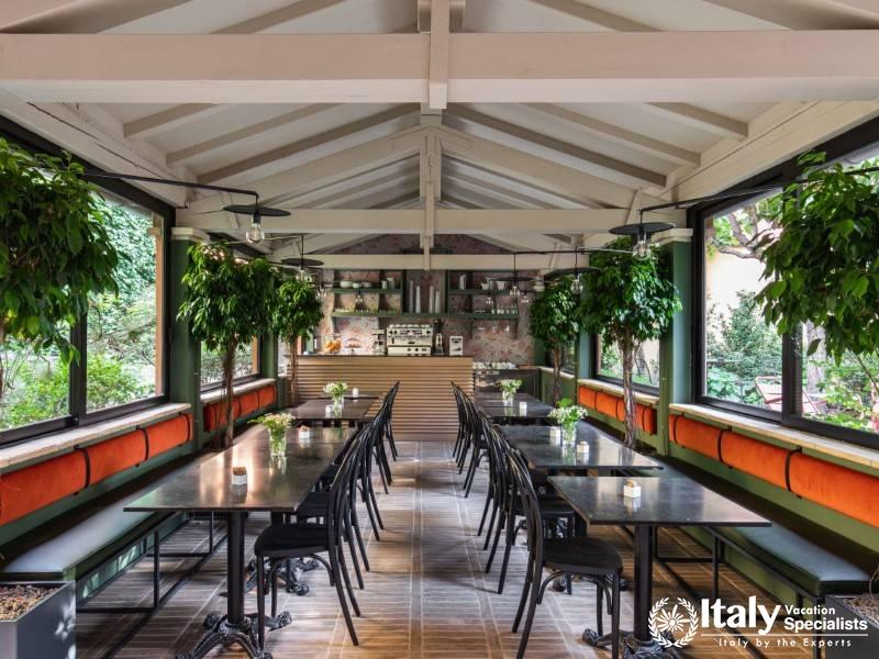 A cozy indoor dining space with modern furniture, plants, and large windows allowing natural light.