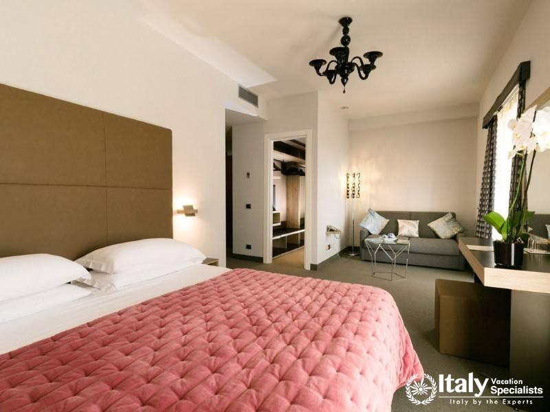 A chic suite with a spacious layout, a soft pink bedspread, and a relaxing seating area with a view.