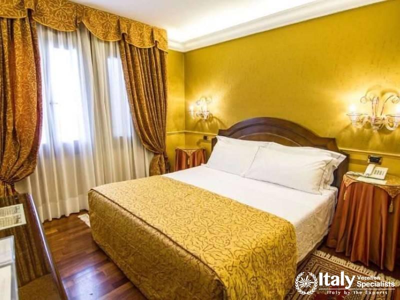 Elegantly draped curtains frame the golden warmth of a double room at Hotel Al Codega.