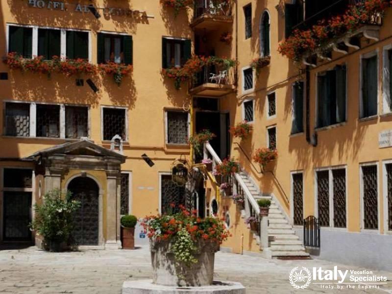 The charming exterior of Hotel Al Codega, with vibrant flowers and a classic Venetian palette.