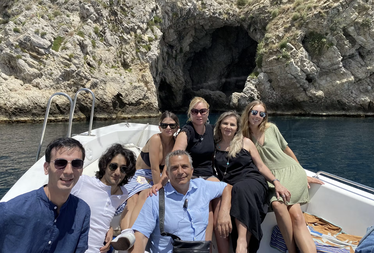 A group of travelers on a boat beside a sea cave on the Italian coast